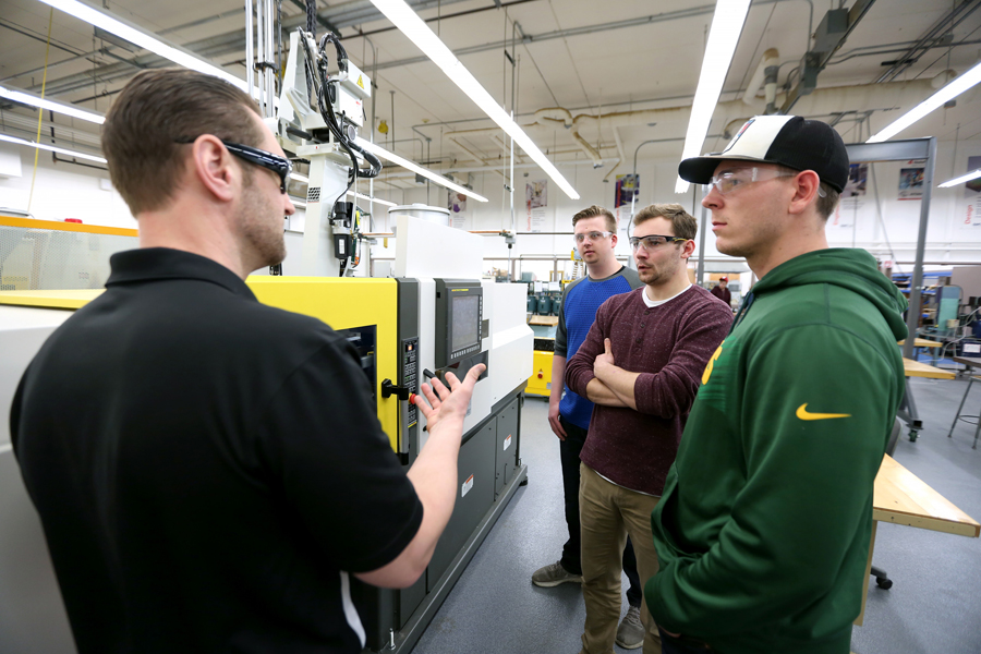 From left, Professor Adam Kramschuster talks with students Hunter Bartz, Bennett Conrardy and Jacob Halling next to a 55-ton Milacron Roboshot injecting molding machine.