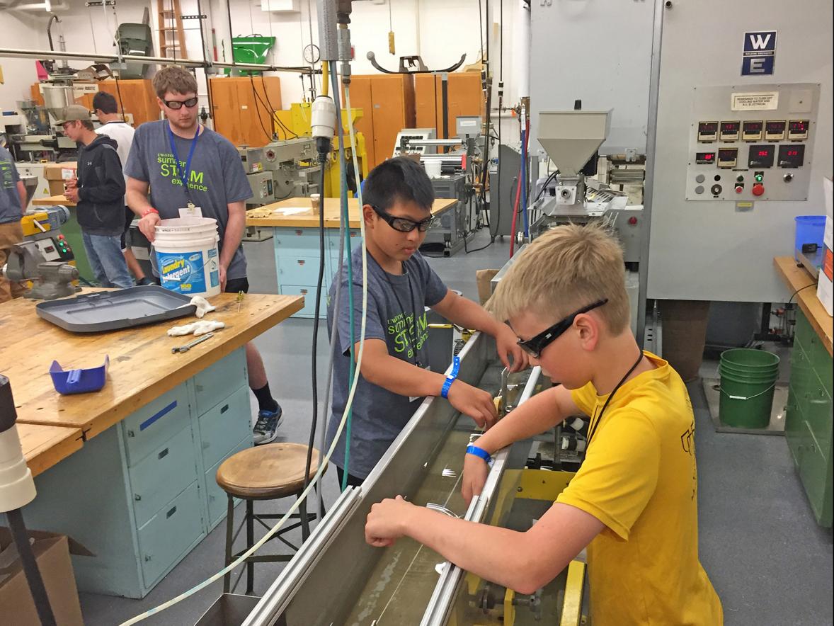 UW-Stout Summer STEAM Experience camp members Ryan Xu, at left, and Tanner Husby, guide filament being extruded for 3D printers in the plastics laboratory on campus.