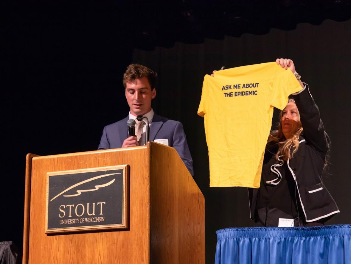 Lauri Badura holds up a t-shirt for an organization she started in memory of her son to help those with drug addiction during the Health Dunn Right conference Tuesday at UW-Stout. Her son, August, at left, also spoke.