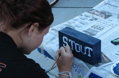 Student painting STOUT on a brick